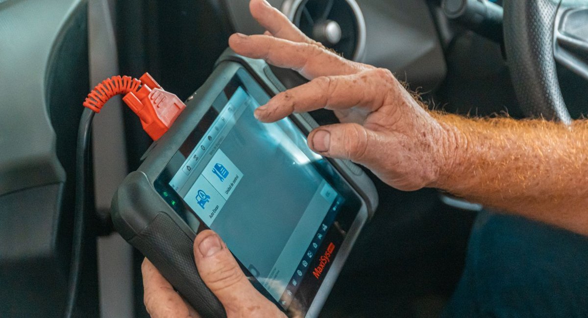 A person uses a diagnostic tablet connected by a cable inside a vehicle.