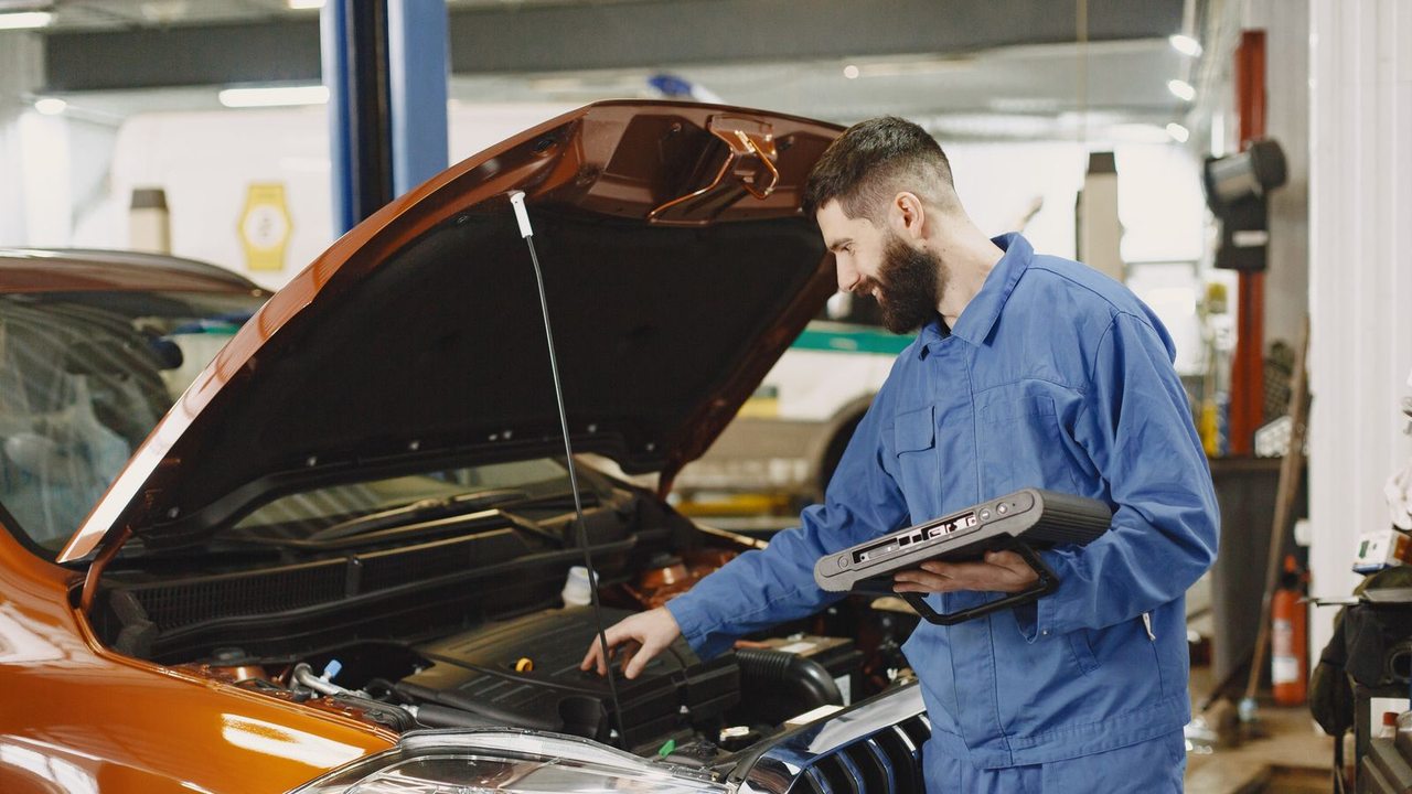 Un professionnel en tenue bleue examine le moteur d’une voiture orange avec un outil de diagnostic.