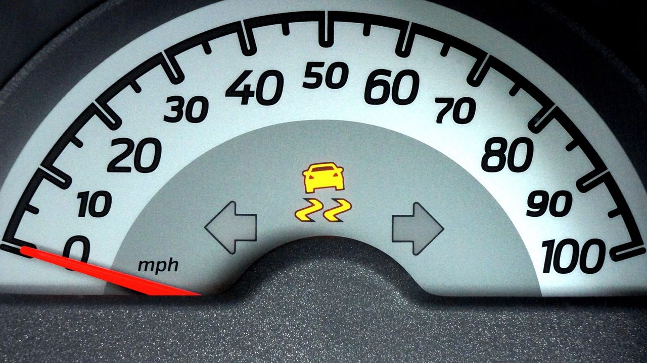 A stationary car’s speedometer with an illuminated yellow stability-control warning light.